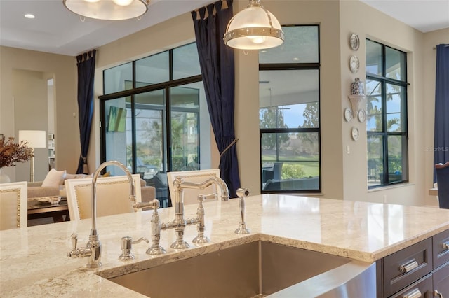 kitchen featuring light stone counters, open floor plan, decorative light fixtures, and a sink