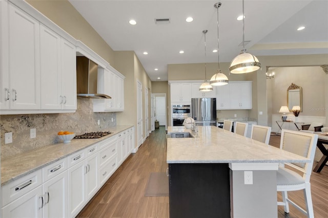 kitchen with decorative light fixtures, stainless steel appliances, a spacious island, wall chimney range hood, and a kitchen breakfast bar