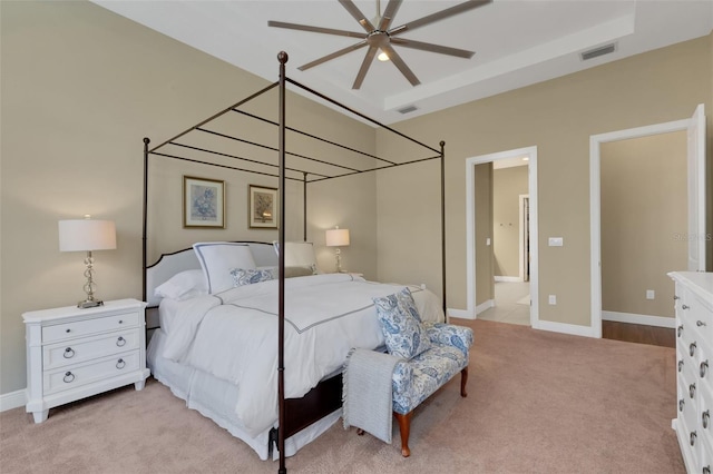 bedroom with a raised ceiling, light colored carpet, visible vents, and baseboards