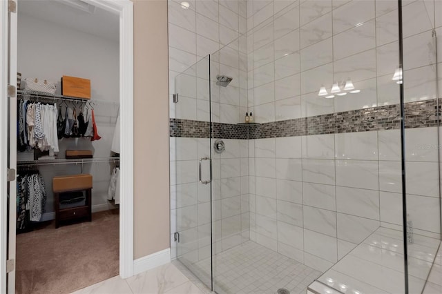 bathroom with marble finish floor, baseboards, a spacious closet, and a shower stall