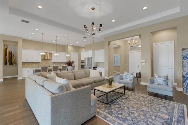 living room with baseboards, visible vents, a raised ceiling, dark wood-style floors, and a notable chandelier