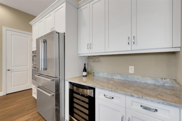 kitchen featuring beverage cooler, white cabinetry, stainless steel appliances, and light stone counters