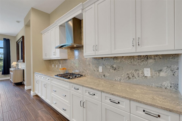 kitchen featuring light stone counters, stainless steel gas stovetop, wood tiled floor, white cabinets, and wall chimney range hood