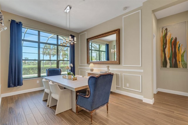 dining space with baseboards, a decorative wall, light wood-type flooring, and an inviting chandelier