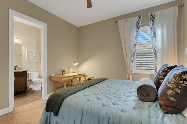 bedroom featuring baseboards, ensuite bathroom, a ceiling fan, and light colored carpet