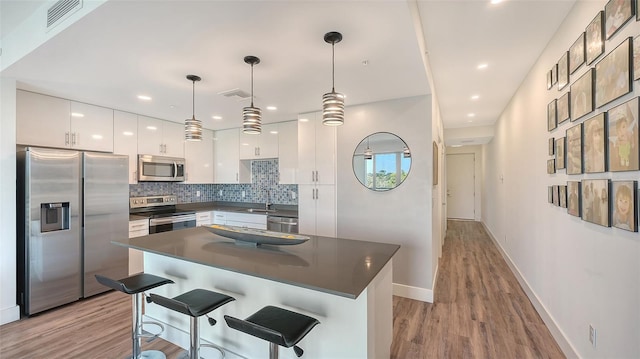 kitchen with dark countertops, appliances with stainless steel finishes, hanging light fixtures, white cabinetry, and a sink