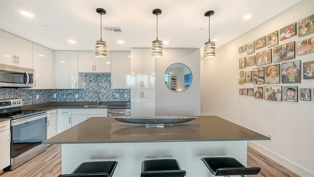 kitchen featuring a kitchen breakfast bar, stainless steel appliances, dark countertops, and white cabinets