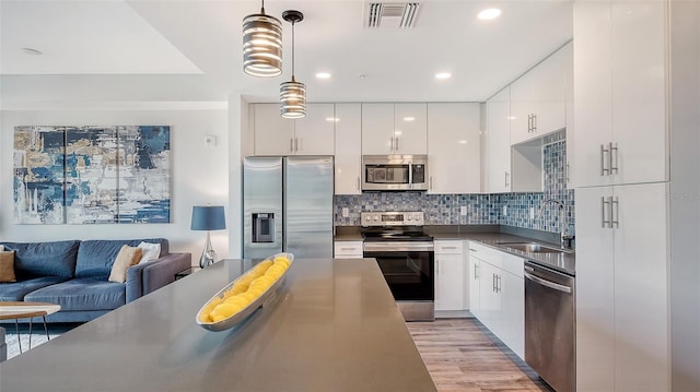 kitchen featuring appliances with stainless steel finishes, dark countertops, white cabinetry, and decorative light fixtures