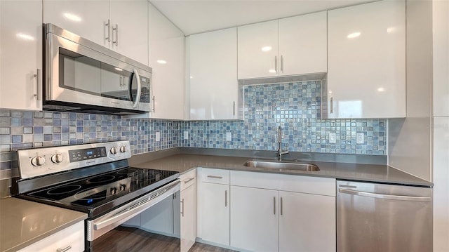 kitchen featuring wood finished floors, a sink, white cabinets, appliances with stainless steel finishes, and tasteful backsplash