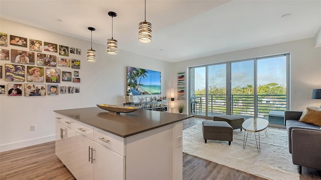 kitchen featuring decorative light fixtures, dark countertops, open floor plan, white cabinetry, and wood finished floors