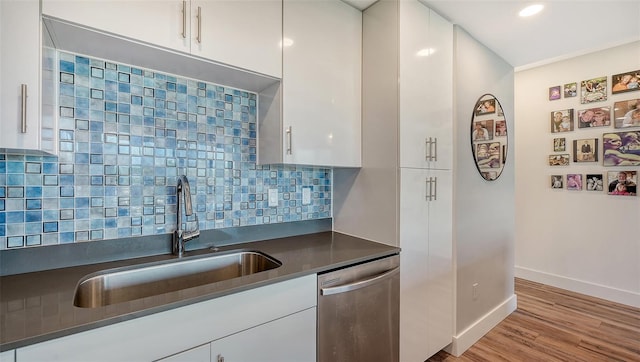 kitchen with dark countertops, stainless steel dishwasher, white cabinets, and a sink