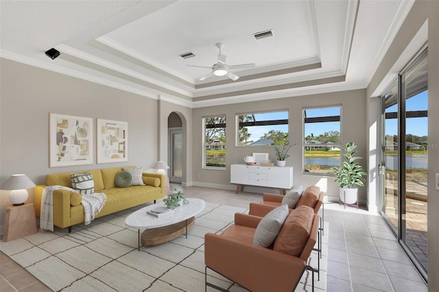 living room with a water view, plenty of natural light, light tile patterned floors, and a tray ceiling