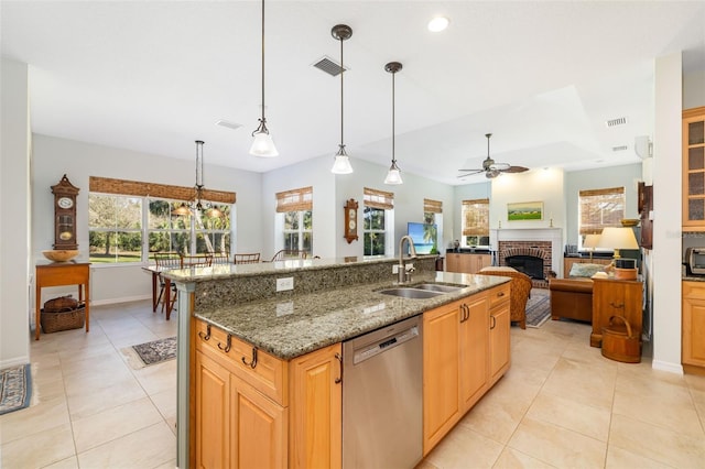 kitchen featuring stone countertops, decorative light fixtures, an island with sink, sink, and stainless steel dishwasher