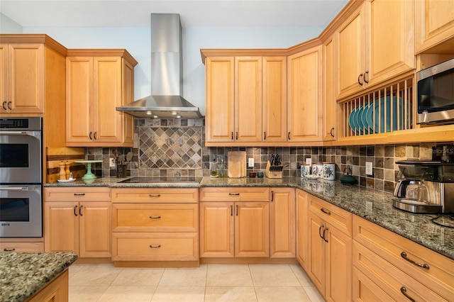 kitchen featuring stainless steel appliances, dark stone countertops, wall chimney range hood, and decorative backsplash