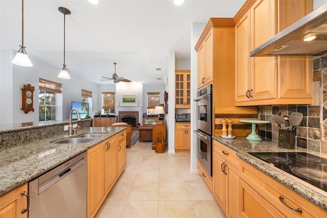 kitchen with pendant lighting, wall chimney range hood, sink, appliances with stainless steel finishes, and light stone counters