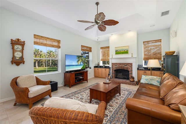 tiled living room with a brick fireplace, a tray ceiling, and ceiling fan