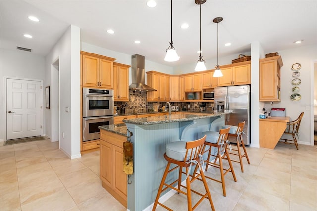 kitchen featuring pendant lighting, ventilation hood, an island with sink, dark stone counters, and stainless steel appliances