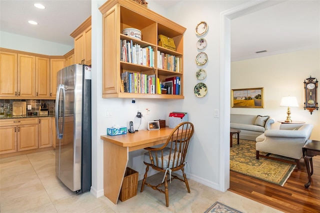 interior space with crown molding, built in desk, light brown cabinets, stainless steel fridge, and decorative backsplash