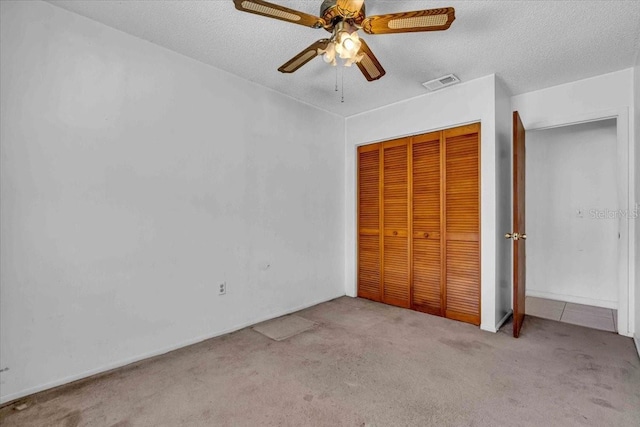 unfurnished bedroom with a textured ceiling, visible vents, a ceiling fan, a closet, and carpet