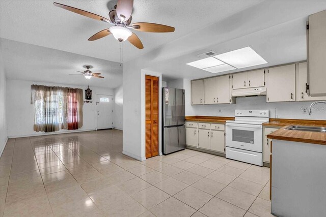 kitchen featuring electric stove, light tile patterned floors, freestanding refrigerator, a sink, and under cabinet range hood