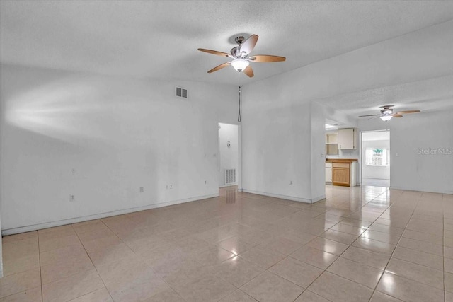 empty room featuring a textured ceiling, light tile patterned floors, visible vents, and a ceiling fan