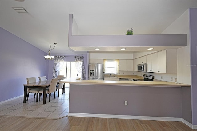 kitchen with decorative light fixtures, stainless steel appliances, light countertops, white cabinets, and a peninsula