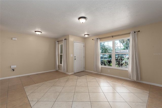 unfurnished room with a textured ceiling, light tile patterned flooring, and baseboards