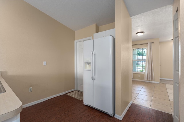 kitchen featuring a textured ceiling, light wood-style flooring, white refrigerator with ice dispenser, baseboards, and white cabinets