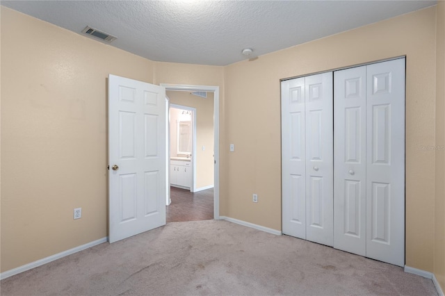 unfurnished bedroom with baseboards, visible vents, light colored carpet, a textured ceiling, and a closet