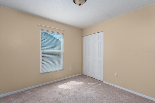 unfurnished bedroom featuring light carpet, a closet, a textured ceiling, and baseboards