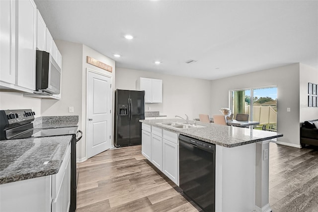 kitchen featuring white cabinetry, a kitchen island with sink, black appliances, sink, and dark stone counters