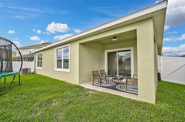 rear view of property with central AC unit, a patio, a trampoline, and a yard