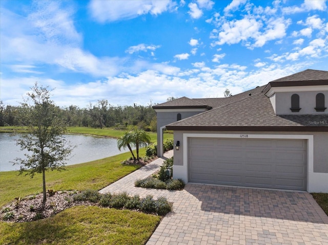 view of front facade featuring an attached garage, a water view, decorative driveway, stucco siding, and a front yard