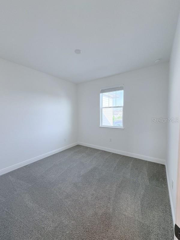 unfurnished room featuring baseboards and dark colored carpet