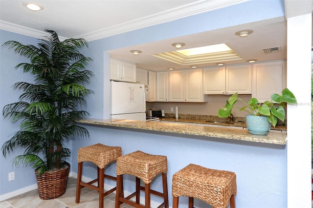 kitchen featuring sink, light stone counters, white refrigerator, ornamental molding, and white cabinets