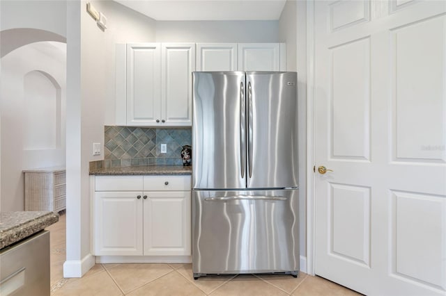 kitchen featuring light tile patterned floors, stainless steel fridge, dark stone counters, decorative backsplash, and white cabinets