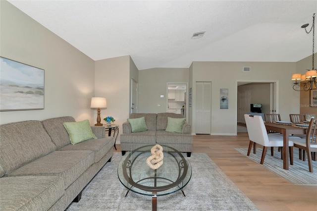 living room featuring lofted ceiling, light hardwood / wood-style floors, and an inviting chandelier