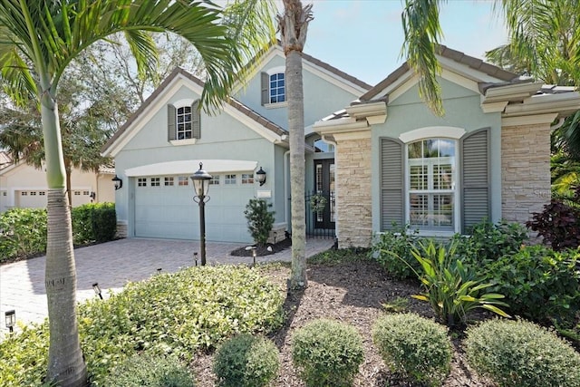 view of front of house featuring a garage, stone siding, decorative driveway, and stucco siding