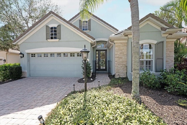 view of front of house featuring an attached garage, stone siding, decorative driveway, and stucco siding