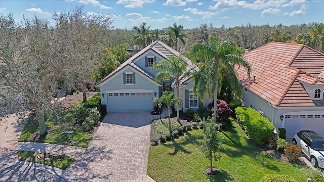 view of front facade featuring an attached garage, a tile roof, decorative driveway, and stucco siding