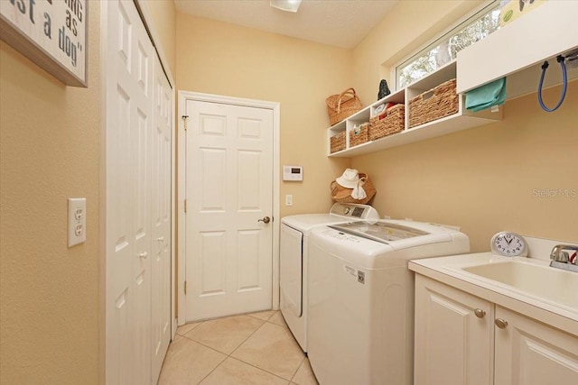 clothes washing area with cabinet space, a sink, washing machine and clothes dryer, and light tile patterned floors