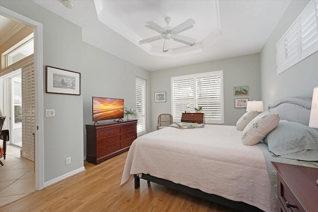 bedroom featuring light wood finished floors, baseboards, a ceiling fan, ornamental molding, and a tray ceiling