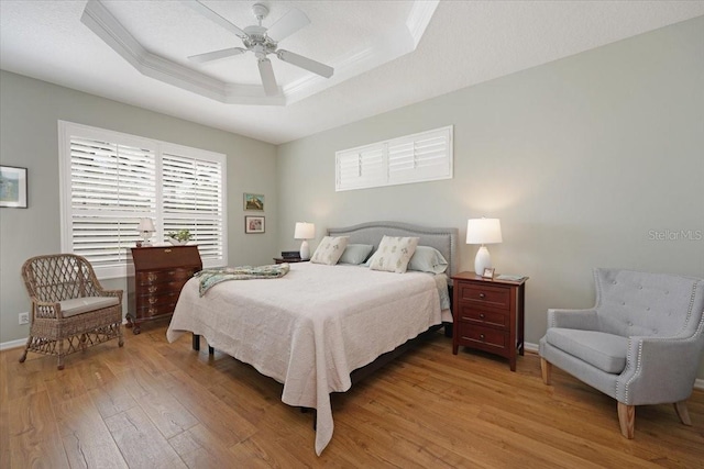 bedroom with light wood finished floors, a raised ceiling, ornamental molding, a ceiling fan, and baseboards