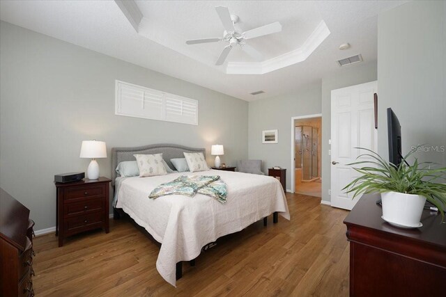 bedroom with ceiling fan, wood finished floors, visible vents, baseboards, and a raised ceiling