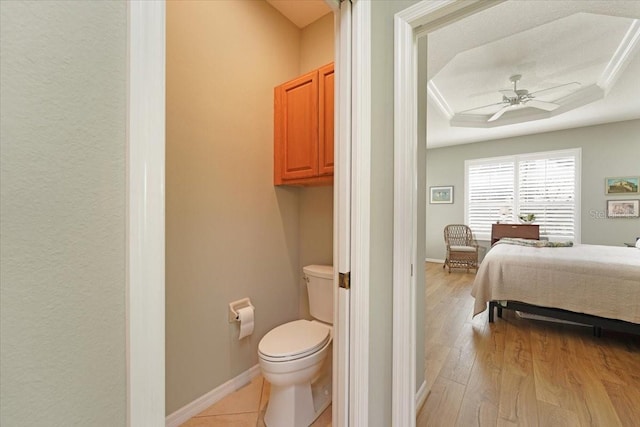 bathroom featuring toilet, wood finished floors, a ceiling fan, baseboards, and a tray ceiling