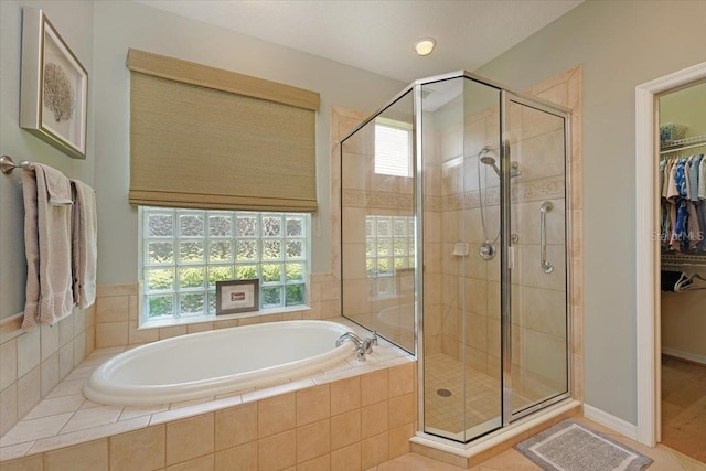 bathroom with a spacious closet, a stall shower, a garden tub, and a healthy amount of sunlight