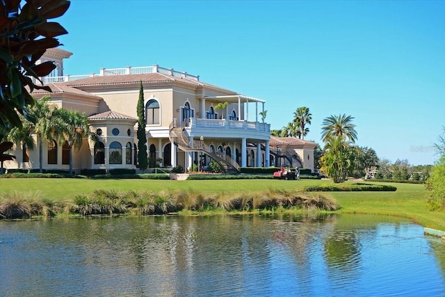 rear view of property featuring stucco siding, a water view, a lawn, stairway, and a tiled roof