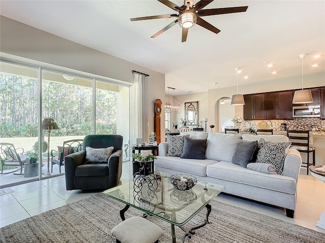 tiled living room with ceiling fan with notable chandelier