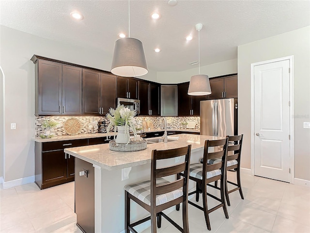 kitchen with dark brown cabinetry, sink, decorative light fixtures, appliances with stainless steel finishes, and an island with sink