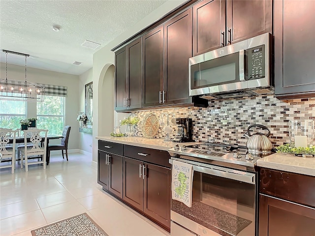 kitchen featuring tasteful backsplash, decorative light fixtures, dark brown cabinets, light tile patterned floors, and stainless steel appliances